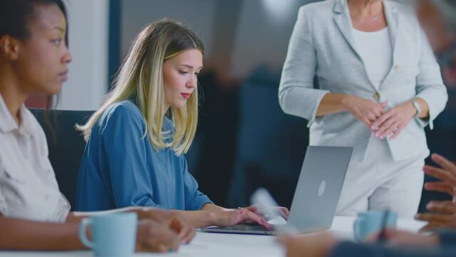 People at department meeting. Young blonde woman typing on laptop computer. Modern open space office interior.