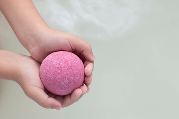 Pink bath bomb in her hands, foaming in the water, close-up. A place to copy