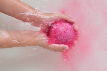 Pink bath bomb in her hands, foaming in the water, close-up. A place to copy