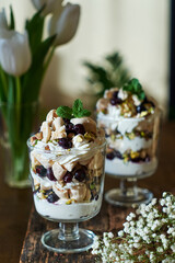 Eton Mess. Trifle with meringue, blueberries, pistachios and mint. Dessert in a glass. Side view. Wooden background.