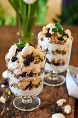 Eton Mess. Trifle with meringue, blueberries, pistachios and mint. Dessert in a glass. Side view. Wooden background.