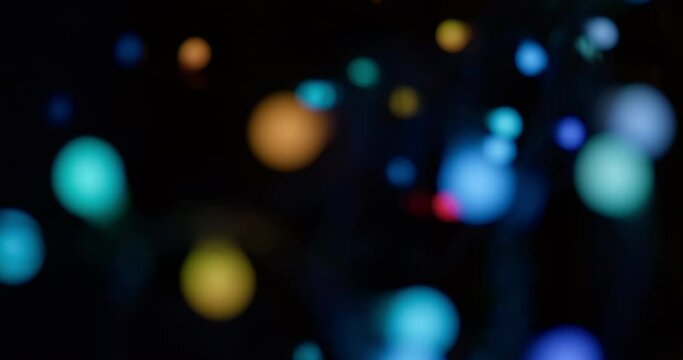 Glowing and blinking defocused multicoloured garland round bokeh lights in the dark. Christmas or holidays festive abstract colorful background