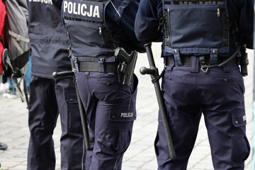 Polscy policjanci w niebieskim mundurze na zabezpieczeniu imprezy w mieście z wyposażeniem służbowym. 