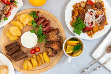 oriental cuisine, barbecue, manti, sausage snacks, salad, fried potatoes on a white table decorated with spices and lemons