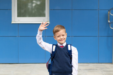 A cute first grader boy in a school uniform with a schoolbag goes to school on a sunny autumn day....