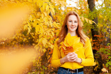 Autumn. red-haired girl in a yellow sweater holds a bouquet of autumn leaves in her hands. Warm tones. Orange. A place for text.