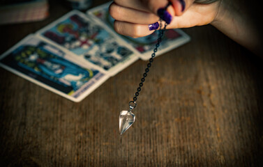 Arm of a dowser with hand-held pendulum on the background of tarot cards. Selective focus.