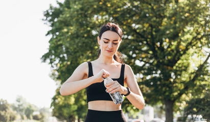 Athletic young woman after runing in the park jogging in the morning for lifestyle health. Female runner standing outdoors holding water bottle. Fitness woman taking a break after running workout.