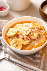 Semolina porridge with syrup and banana. Sweet breakfast, baby food. Semolina porridge in a white bowl on a gray concrete background.