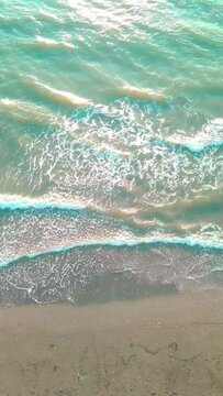 Drone view of the beautiful waves on the sandy beach, the sea waves break on the sandy coastline. Aerial photography of the beach with black sands. Green water. vertical video