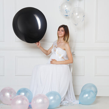 Young pregnant woman sitting on a chair, holding a big black balloon. Concept of a reveal gender party.