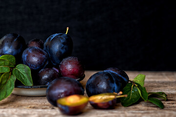 Ripe plum with green leaves on rustic background. Ripe fresh organic plums.