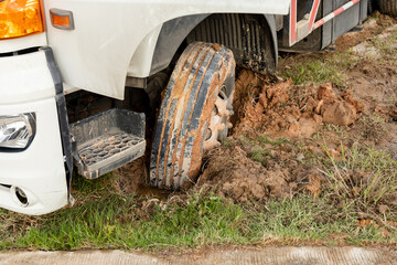 Fototapeta na wymiar Wheel of a heavy truck lorry stuck in deep mud soft ground. Muddy and soft soil road at construction site after raining.