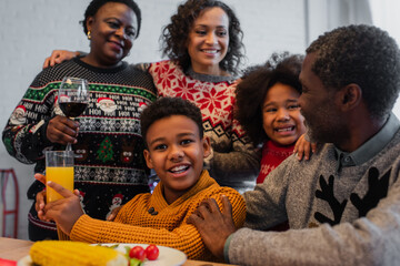 happy african american boy with orange juice near family on christmas dinner