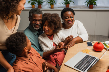 cheerful african american man pointing at laptop near family on thanksgiving day