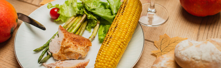 top view of grilled corn and turkey fillet near asparagus and lettuce on plate, banner