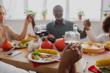 selective focus of african american woman and boy holding hands while praying with blurred family near served table