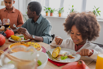 african american girl having thanksgiving dinner near blurred grandpa and brother
