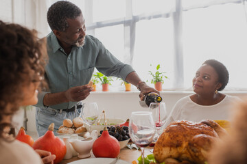 Mature african american man pouring wine near family during thanksgiving celebration