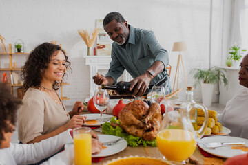 African american man pouring wine near family and thanksgiving dinner