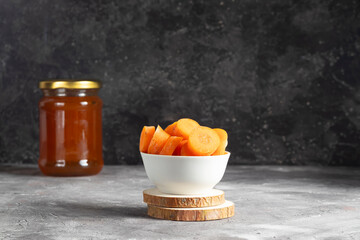 A plate with sliced juicy carrots on a background with a glass jar with sweet confiture on a dark background