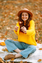 Fototapeta premium Glowing sparkles in hands. Young woman in a yellow sweater with Christmas sparklers on nature. Autumn style. 