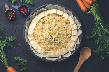 Homemade pie with sauerkraut or pickled cabbage, carrots and greenson dark rustic kitchen table background, preparation, top view. Vegetarian clean food. Healthy eating concept