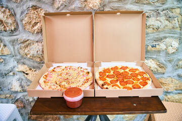 Two fresh pizzas ham with mushrooms and pepperoni in a box with tomato sauce. High quality photo