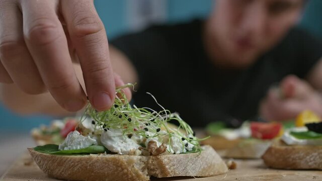 Young man is cooking in the kitchen aperitive. Lays microgreens on bruschetta.