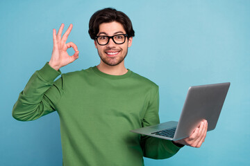 Portrait of smiling geek nerd young businessman in glasses show okay sign hold laptop isolated on...