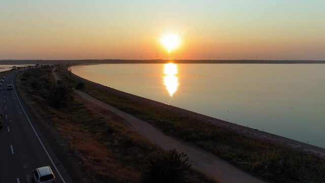 drone flying over firth at dusk, aerial view over sea and road on background of charming landscape with windmills, passing cars by at sunset