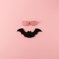Minimalistic Halloween happy face made of pink sunglasses and black bat on pink background. Creative funny Halloween concept. Top view.
