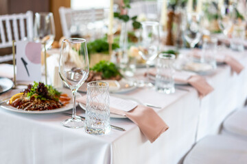 Wine glasses, flowers, fork, knife served for dinner in restaurant with cozy interior