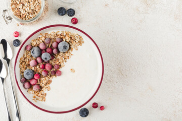Greek yogurt with granola, fresh blueberries, cranberries and mint in a plate and two spoons on a light background.