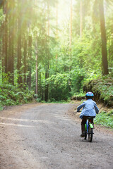 Obraz premium a small child in a helmet learns to ride a two-wheeled bicycle on forest paths. joint time of parents and children, active recreation