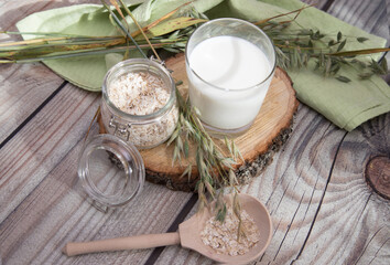 An alternative to traditional milk is vegan oat milk in a glass with oat flakes and spikelets on a wooden background. Vegan product