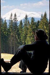 The silhouette of a man sitting on the threshold of a mountain hut with beautiful views of...