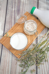A substitute for animal milk is a glass of oat milk with oat spikelets and oats in a glass jar on a wooden stand. Vegan product