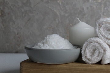 salt for bath scrub home body care. Coarse salt lies in a gray bowl plate with a wooden spoon towel candle on a gray background. Spa relaxation