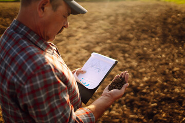 Farmer watching some charts and checks quality of soil. Agriculture, gardening, business or ecology...