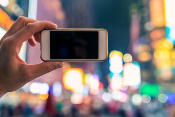 Hand holds a phone in Times Square New York City by night