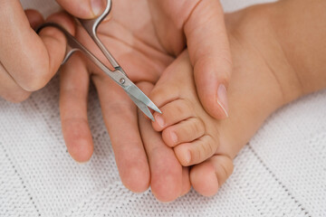 Mom cuts toenails of a newborn baby with metal scissors. Selective focus