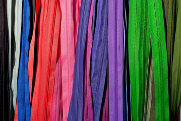 Multicolored zipper locks in a clothing store. Many colored strips of fabric hang on the wall. Clothing accessory close up.