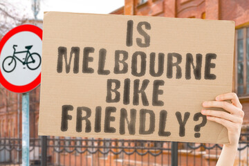 The question " Is Melbourne bike friendly? " on a banner in men's hand with blurred background. Transportation. Zero waste. Bicycle lane. Streets. City. Safety. Insecure. Road signs. Dangerous