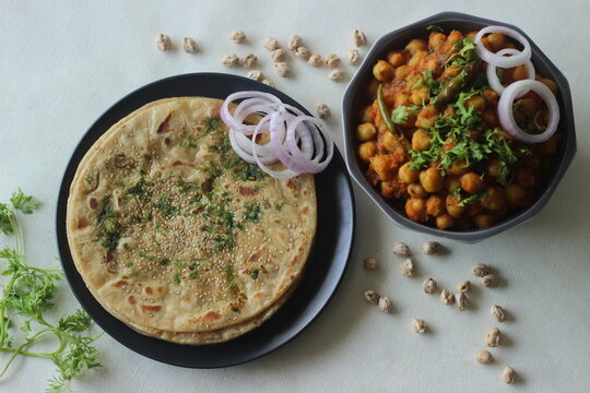 Perfectly round Paratha. Indian flatbread made of wheat flour topped with sesame seeds and coriander leaves served with white chickpea gravy commonly known as chole masala
