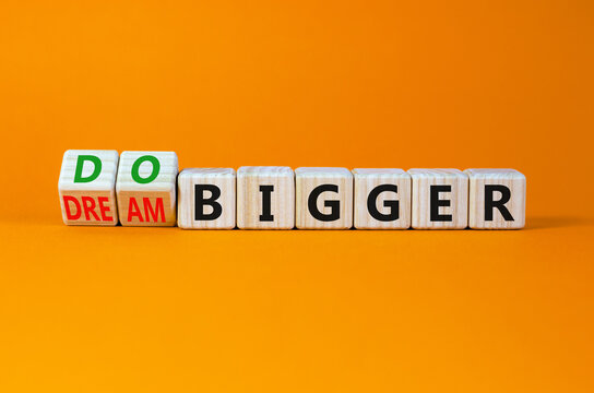 Dream and do bigger symbol. Turned wooden cubes and changed words dream bigger to do bigger. Business and dream and do bigger concept. Beautiful orange background, copy space.