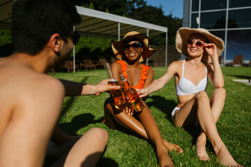 Cheerful friends drink beer near the pool
