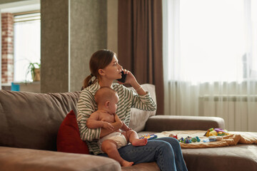 Woman talking on mobile phone holding baby on her knees