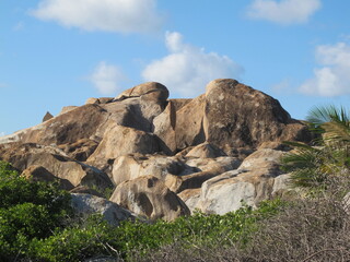 Beige and brown boulders against a blue sky with clouds. Rocks and green vegetation. Stoney bay, Virgin Gorda, British Virgin Islands, Caribbean
