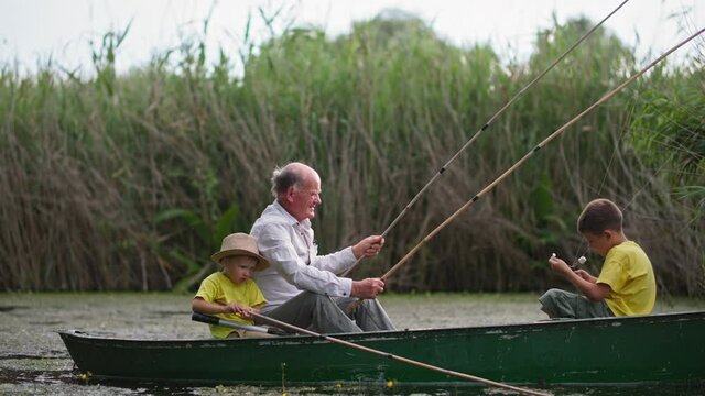 family weekend at pond, fisherman puts on glasses to untangle the fishing rods while sitting in the boat with his grandchildren